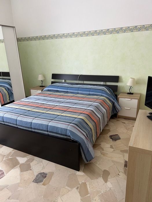 Camera 3: letto matrimoniale con copriletto a righe, comodini con lampade, pavimento in marmette